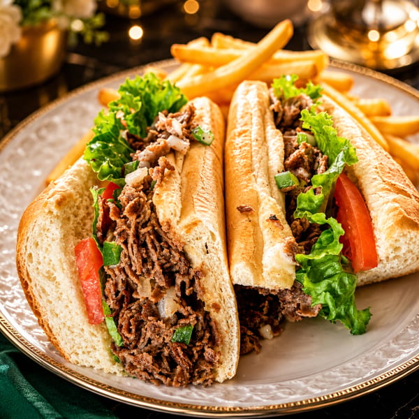 Two steak subs with lettuce, tomato, and onions, served with a side of golden fries.