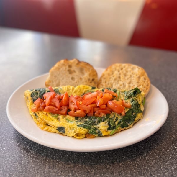 Spinach and tomato omelet with two English muffin halves on a white plate at a diner.