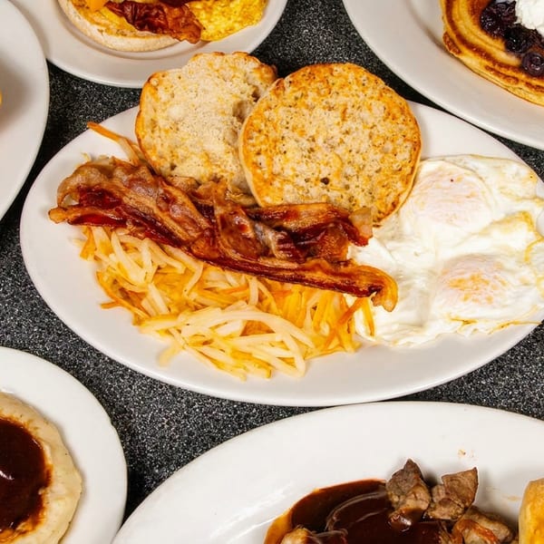 Overhead view of multiple plates with breakfast, grilled cheese, pancakes, and a cheeseburger.