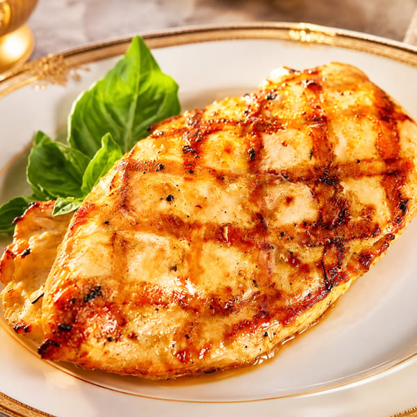 Grilled chicken breast with grill marks and fresh basil on a white plate with gold trim.