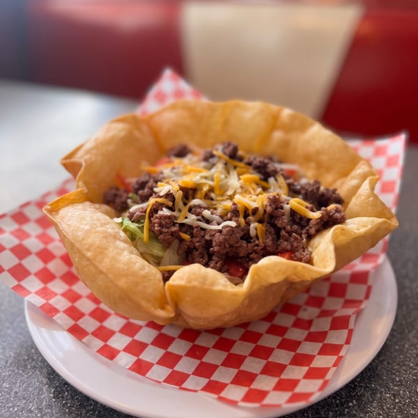 Taco salad in a crispy tortilla bowl, topped with ground beef, cheese, and lettuce.
