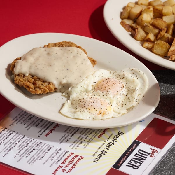 A diner breakfast with chicken fried steak, eggs, hash browns, toast, and coffee on a red table.