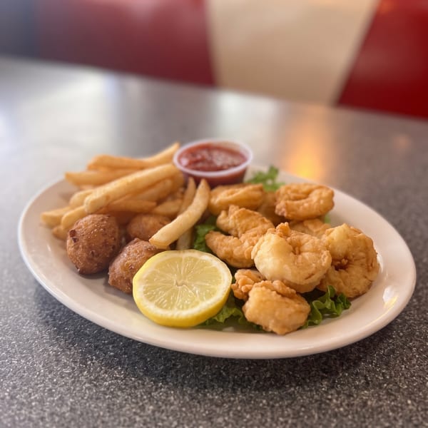 Fried shrimp, french fries, hush puppies, and a lemon wedge on a white plate.