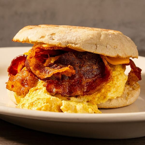 Breakfast sandwich with crispy bacon, scrambled eggs, and cheese on an English muffin.
